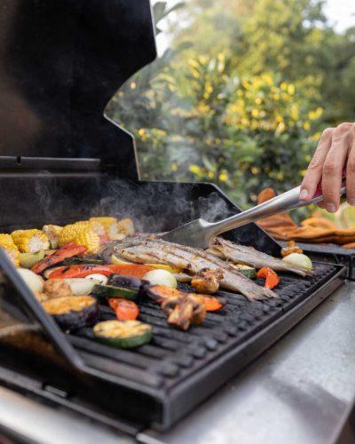 People grilling fish and corn on a modern grill outdoors at sunet, close-up. Cooking food on the open air